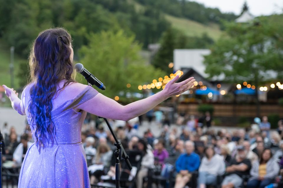 A woman standing on the Subaru Stage, singing classical opera music to the Village audience.