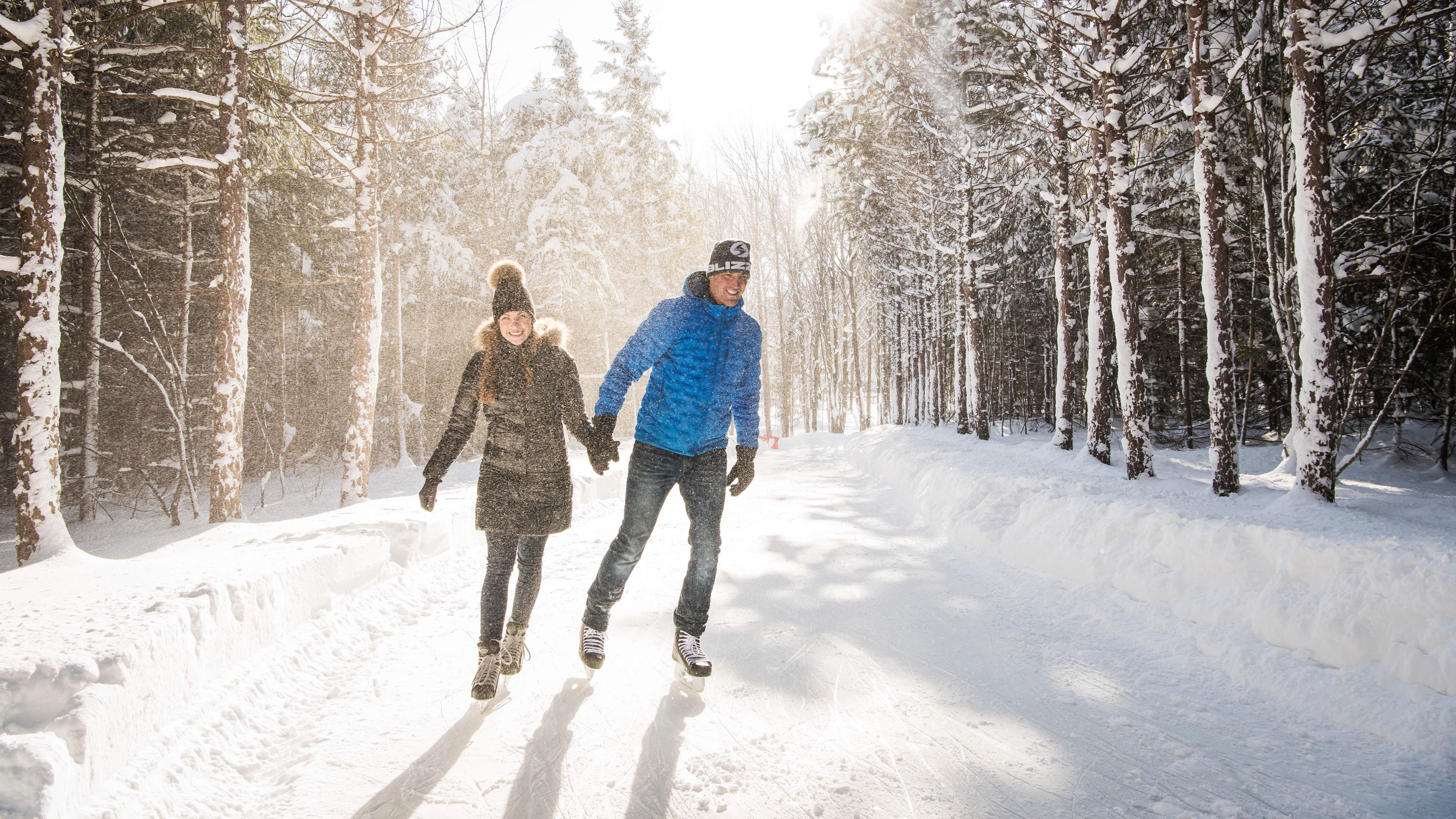 Couple holding hands and skating around the 1.1km ice skating loop at the top of the Mountain on a snowy winter's day.