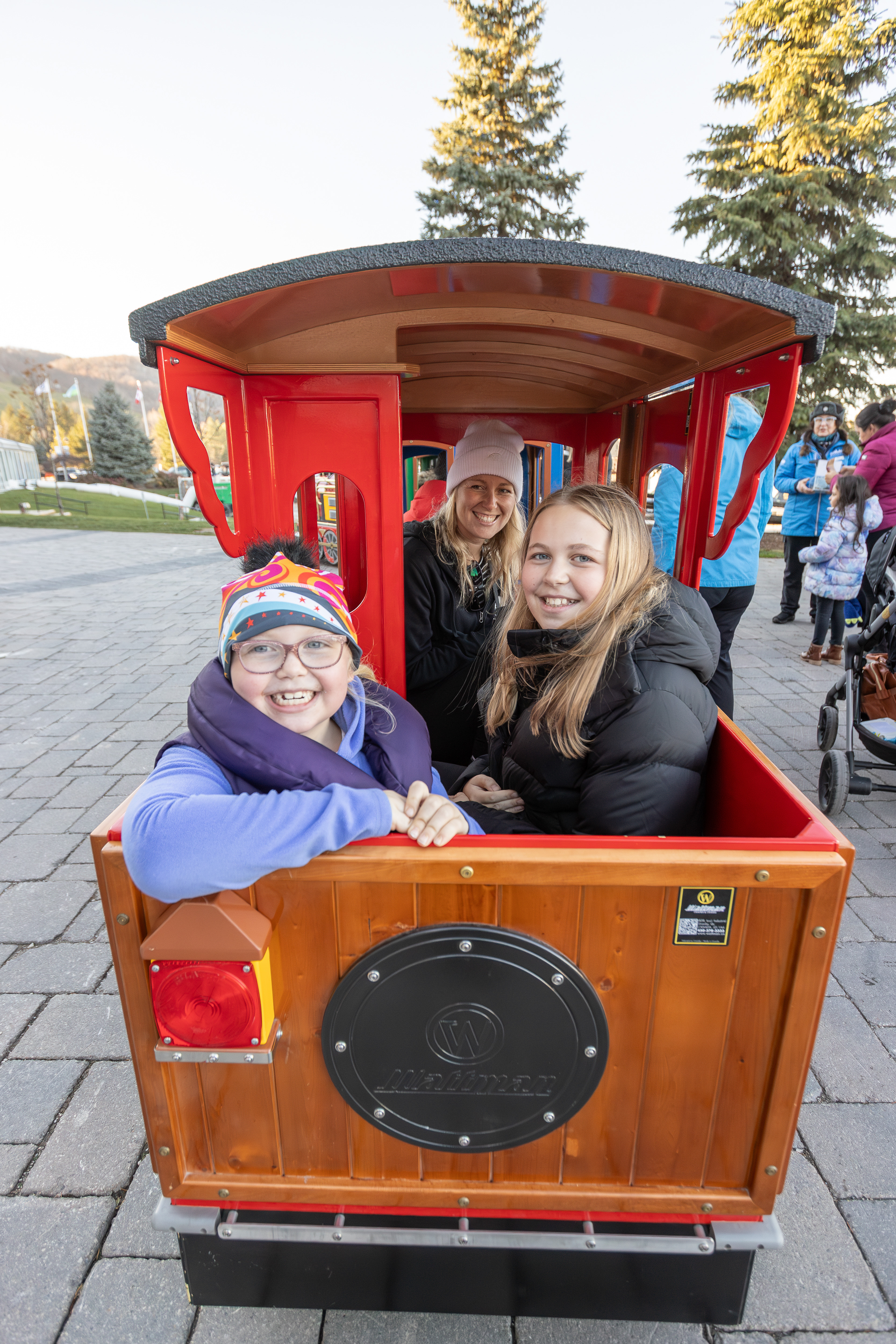 Mom and two daughters sitting in the caboose, taking a ride through the Village on the Holiday Express trackless train during Holiday Magic.