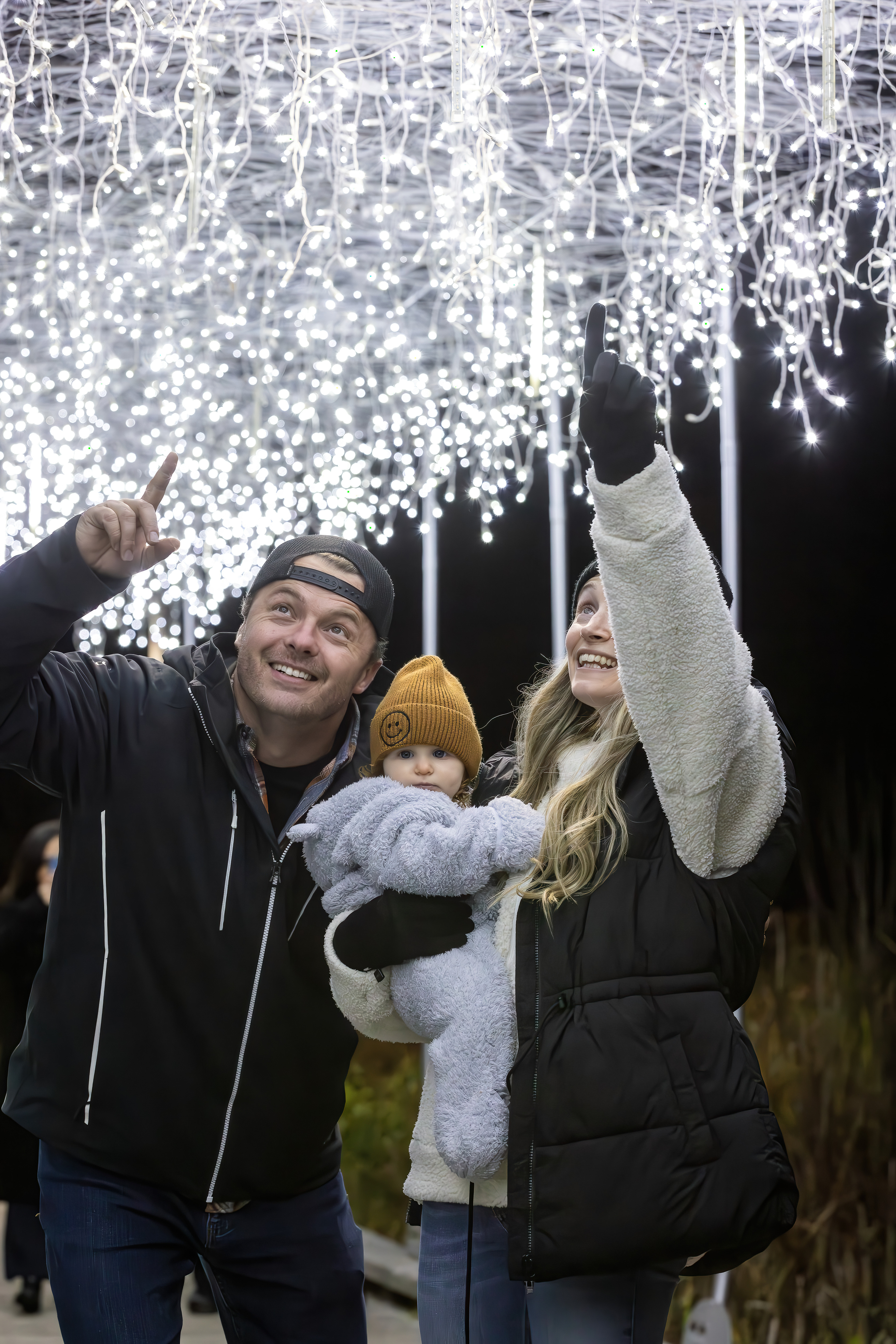Parents with young baby pointing to show the baby the dangling Holiday Magic Lights.