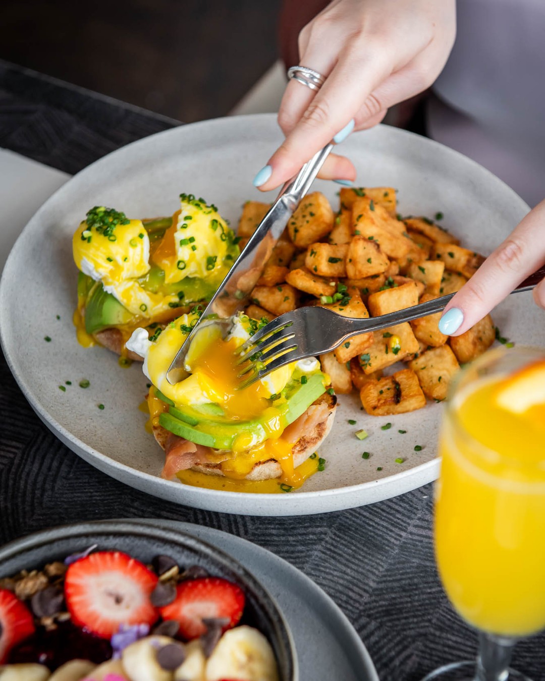 Guest breaking the yolk on their avocado eggs benedict at Oliver & Bonacini Café Grill, located in the Westin Trillium House.