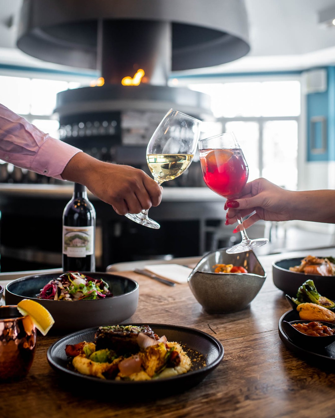 Couple cheersing wine glasses over a table full of beautifully prepared dishes at Oliver & Bonacini Café Grill, located in the Westin Trillium House.