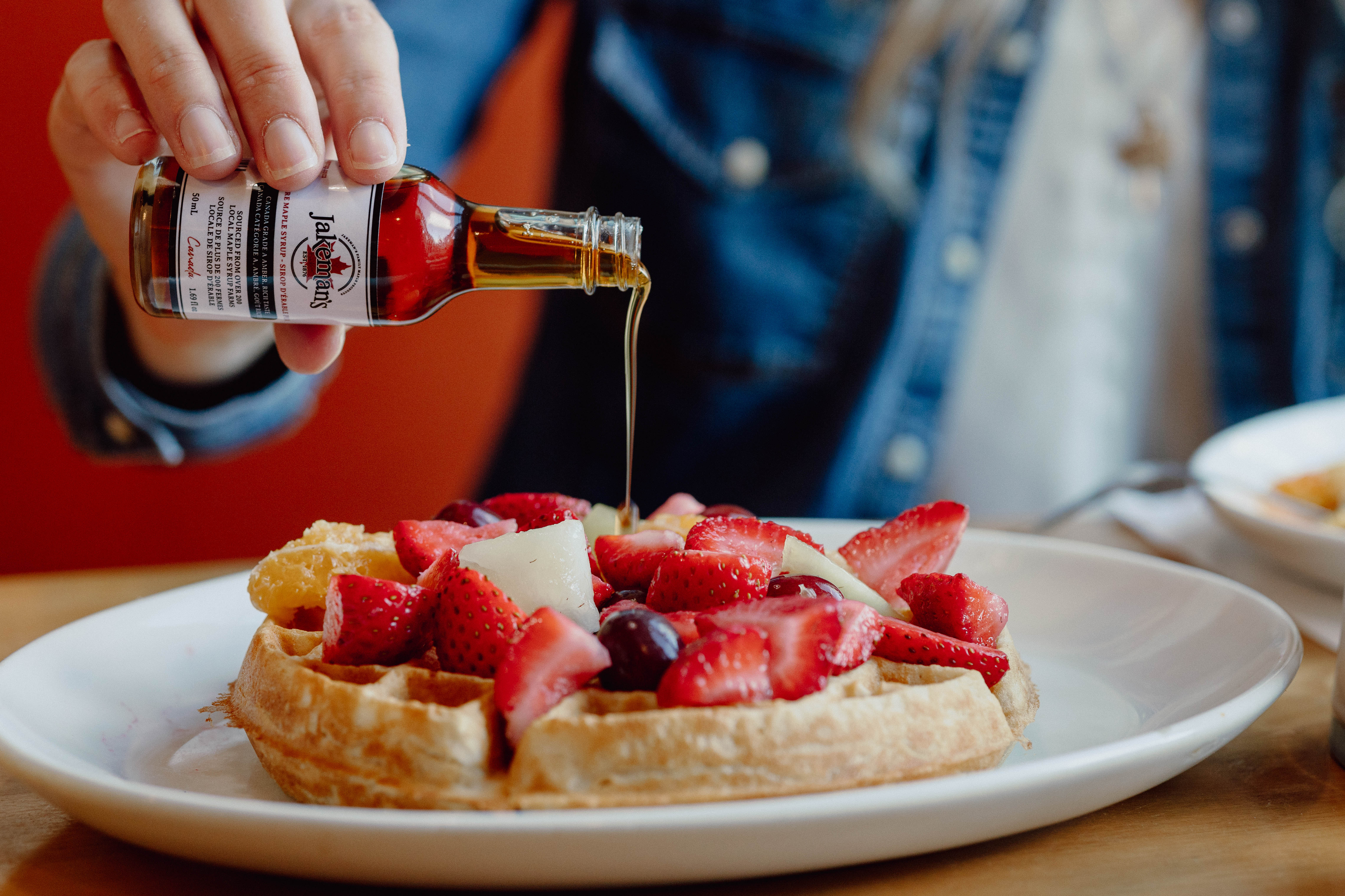 Hand pouring true Canadian Maple Syrup over a plate of warm waffles topped with fresh berries.