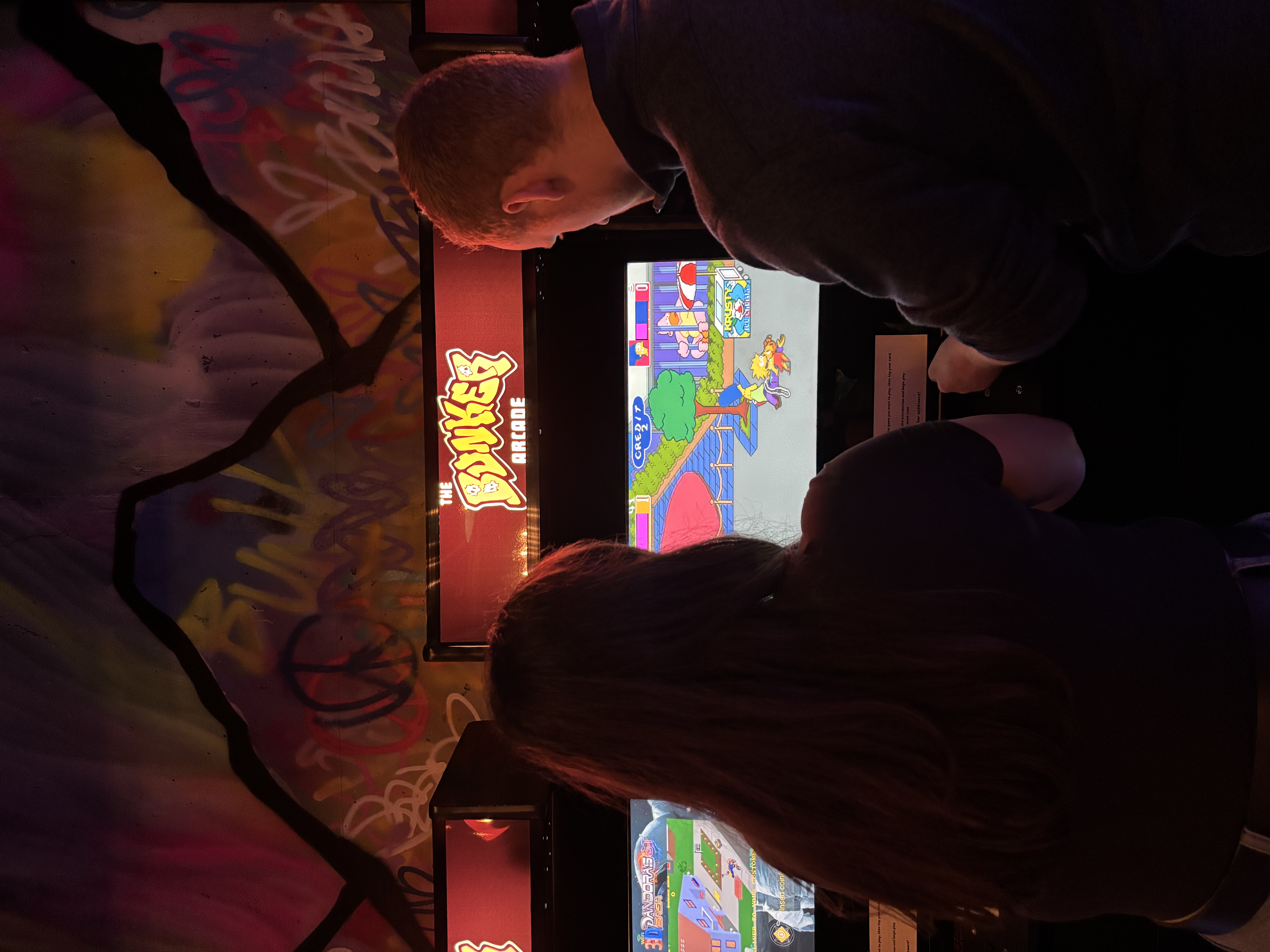 Couple battling it out playing The Simpsons on a retro arcade console at The Bunker Arcade. 