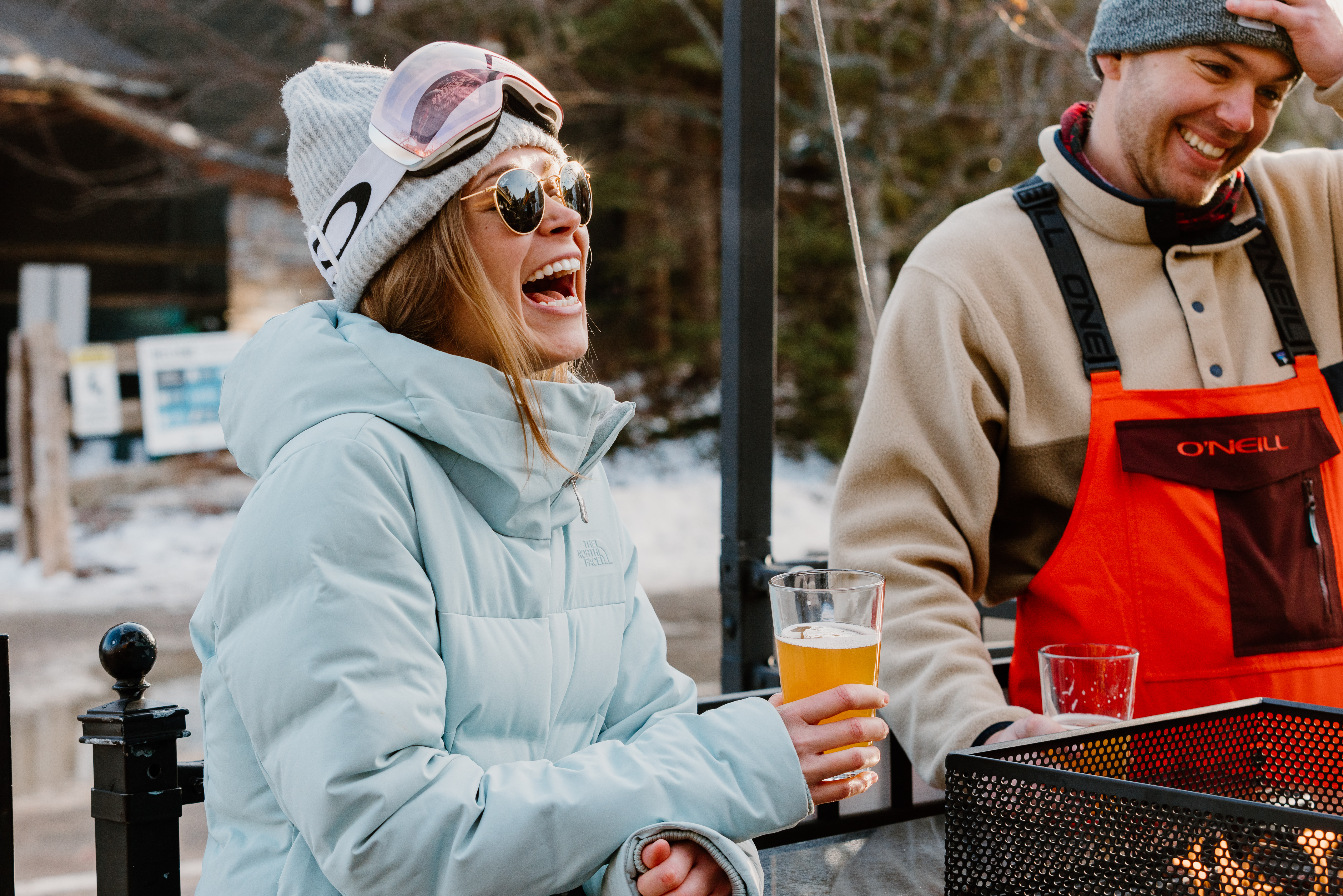 Woman dressed in ski suite and googles enjoying a pint of beer on the Rusty's at Blue patio. 