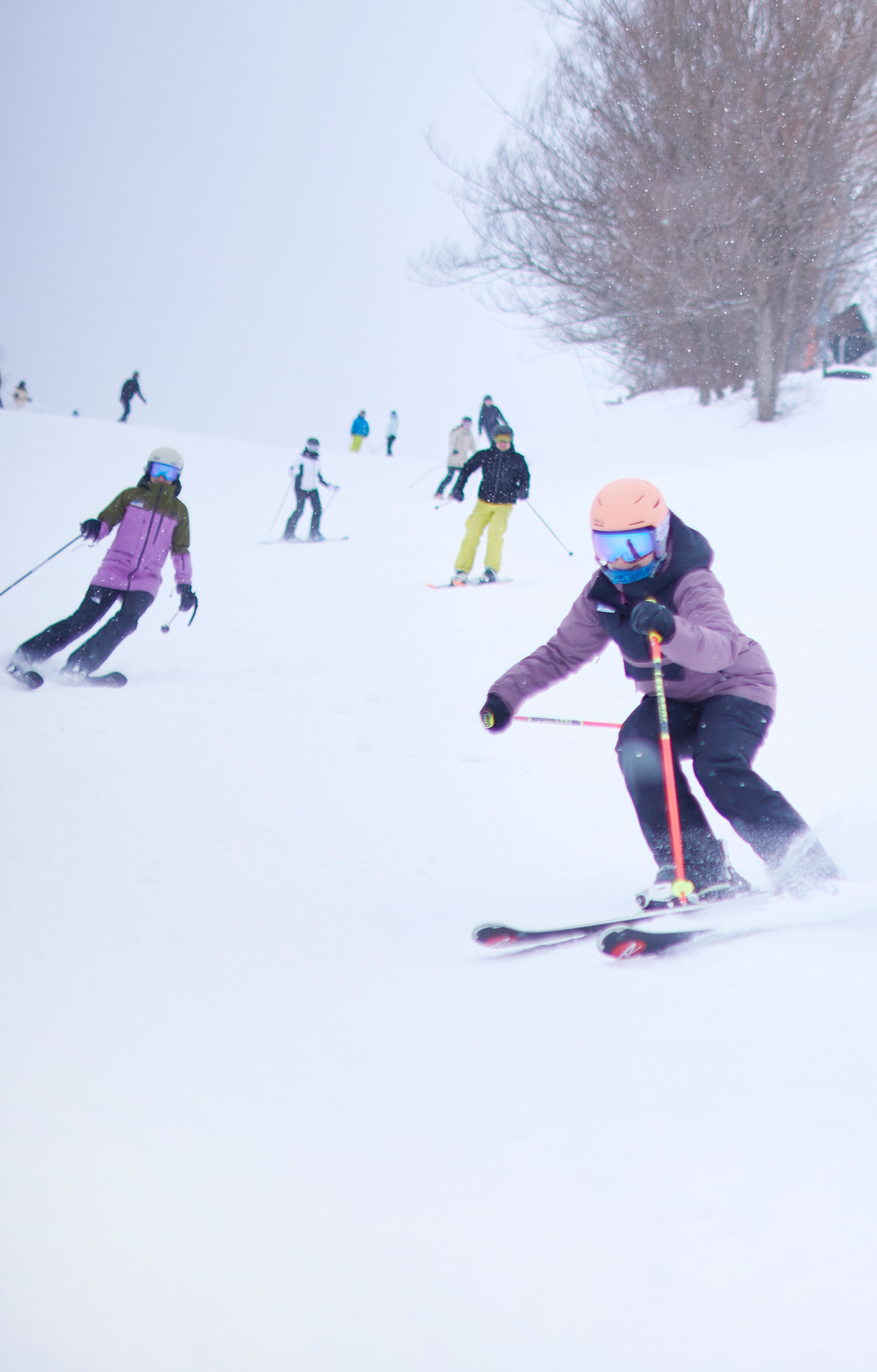 Group of friends race each other down the ski slopes on a snowy Winter afternoon.