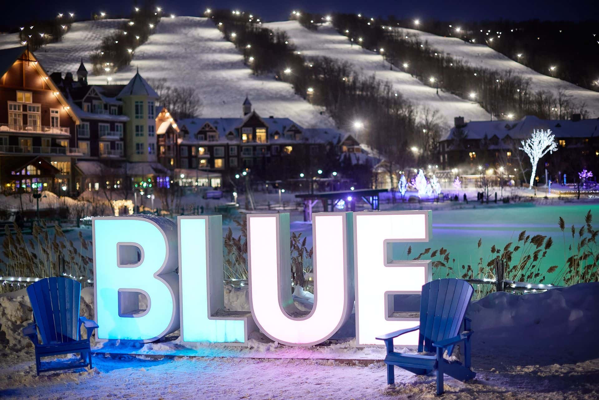 The Blue Sign lit up at night, with the village and mountain displayed in the background. 