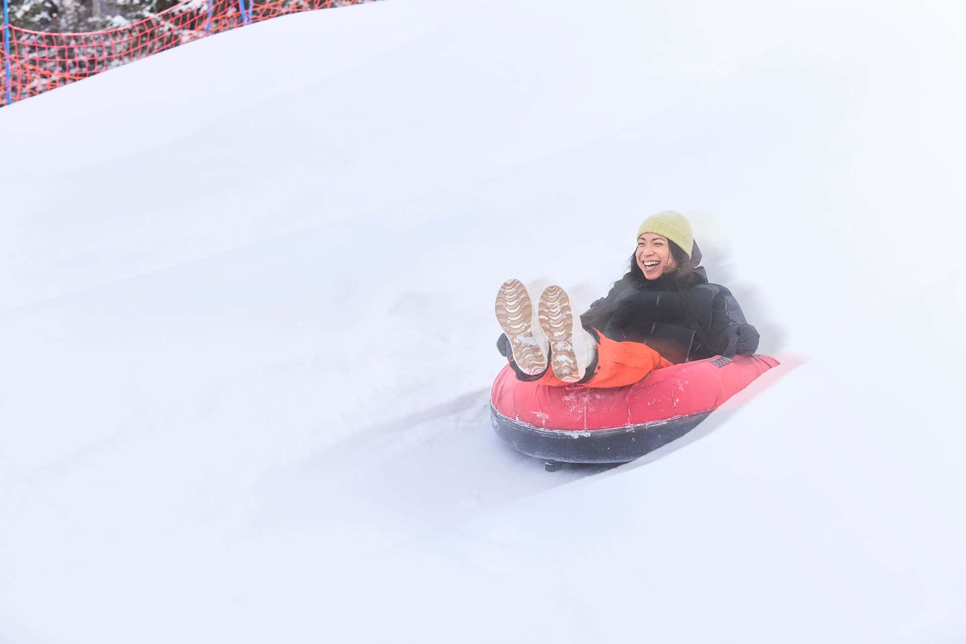 Woman in a snow tube, smiling wide as she speeds down the snow covered slope.