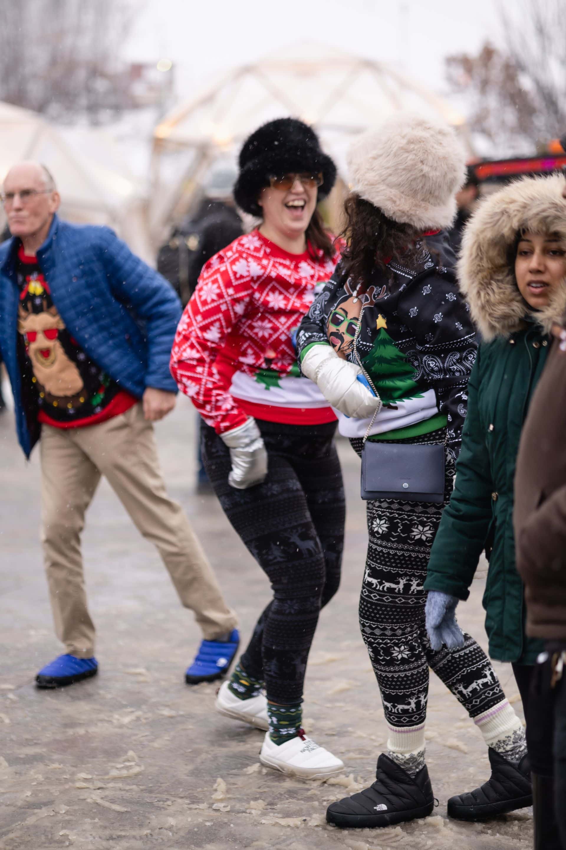Friend dressed in Christmas sweaters and fur hats, dancing to Caribbean music in the Village events plaza.