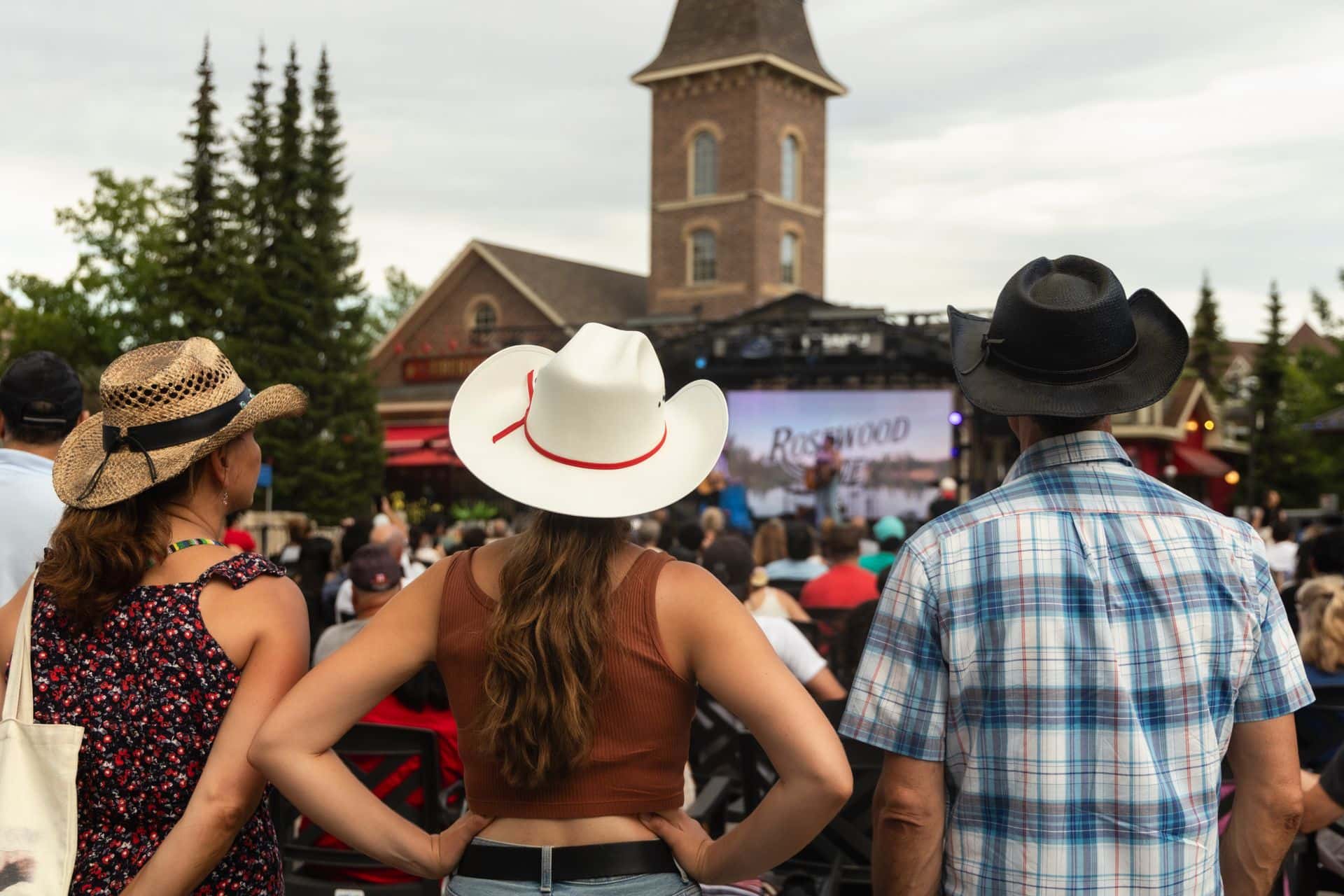 3 country music lovers dressed in their cowboy best enjoying live performances at Country Fest in the Village.