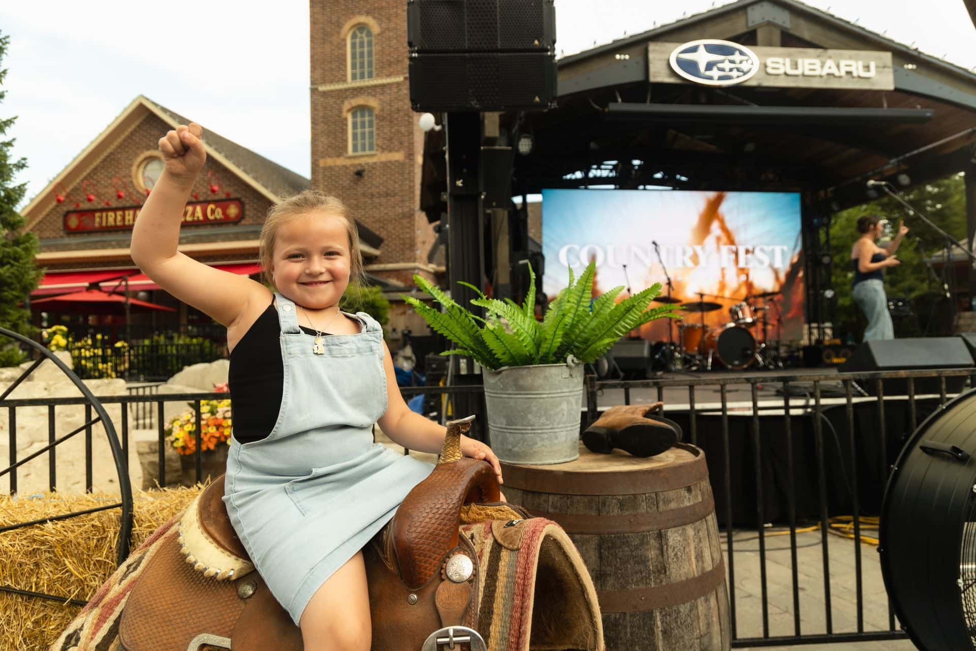 A young girl posing like a country cowgirl on a horse saddle in front of the Subaru Stage.
