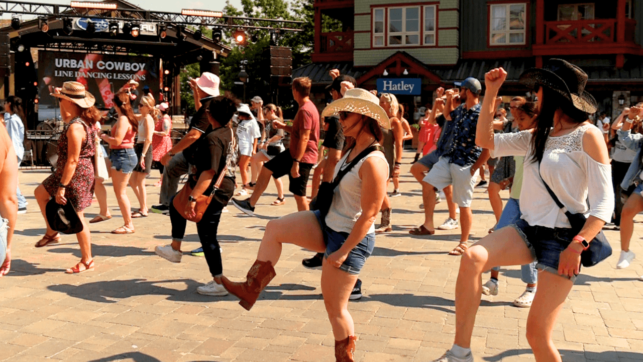 Lively crowd following along with Urban Cowboy Line Dancing Lessons in the Village Plaza.