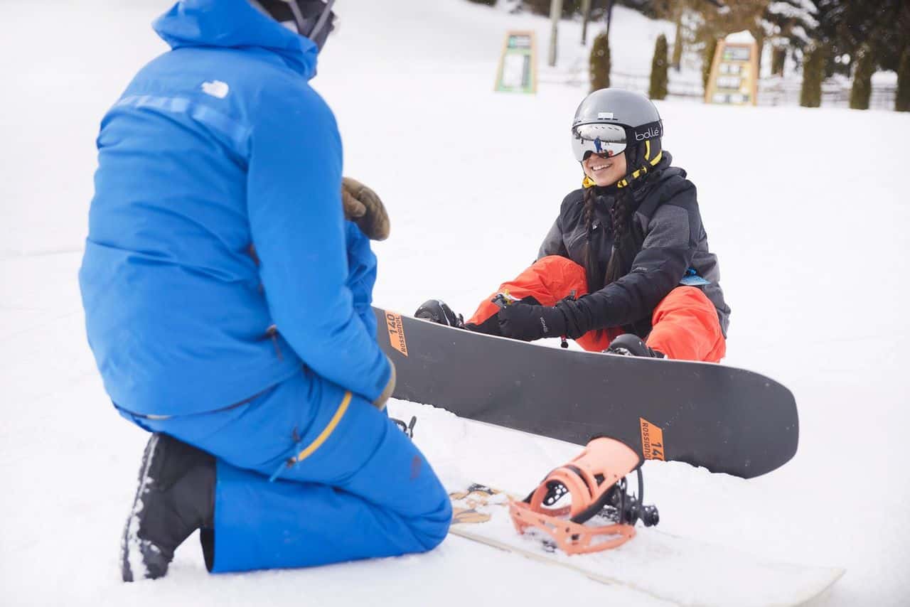 A beginner snowboarder does up her bindings. 