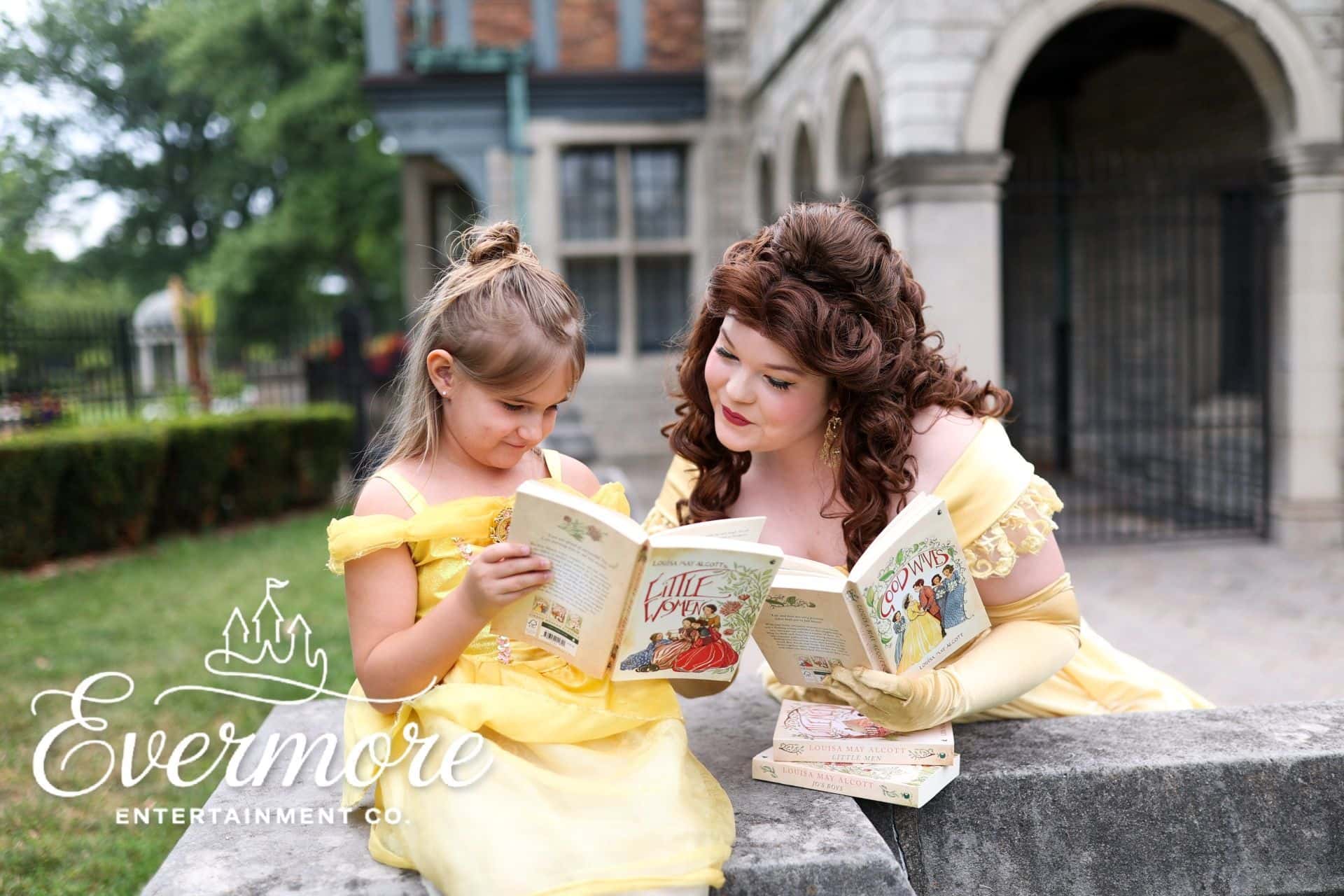 Performer and young girl each dressed up as fairytale princesses while the performer reads to her.