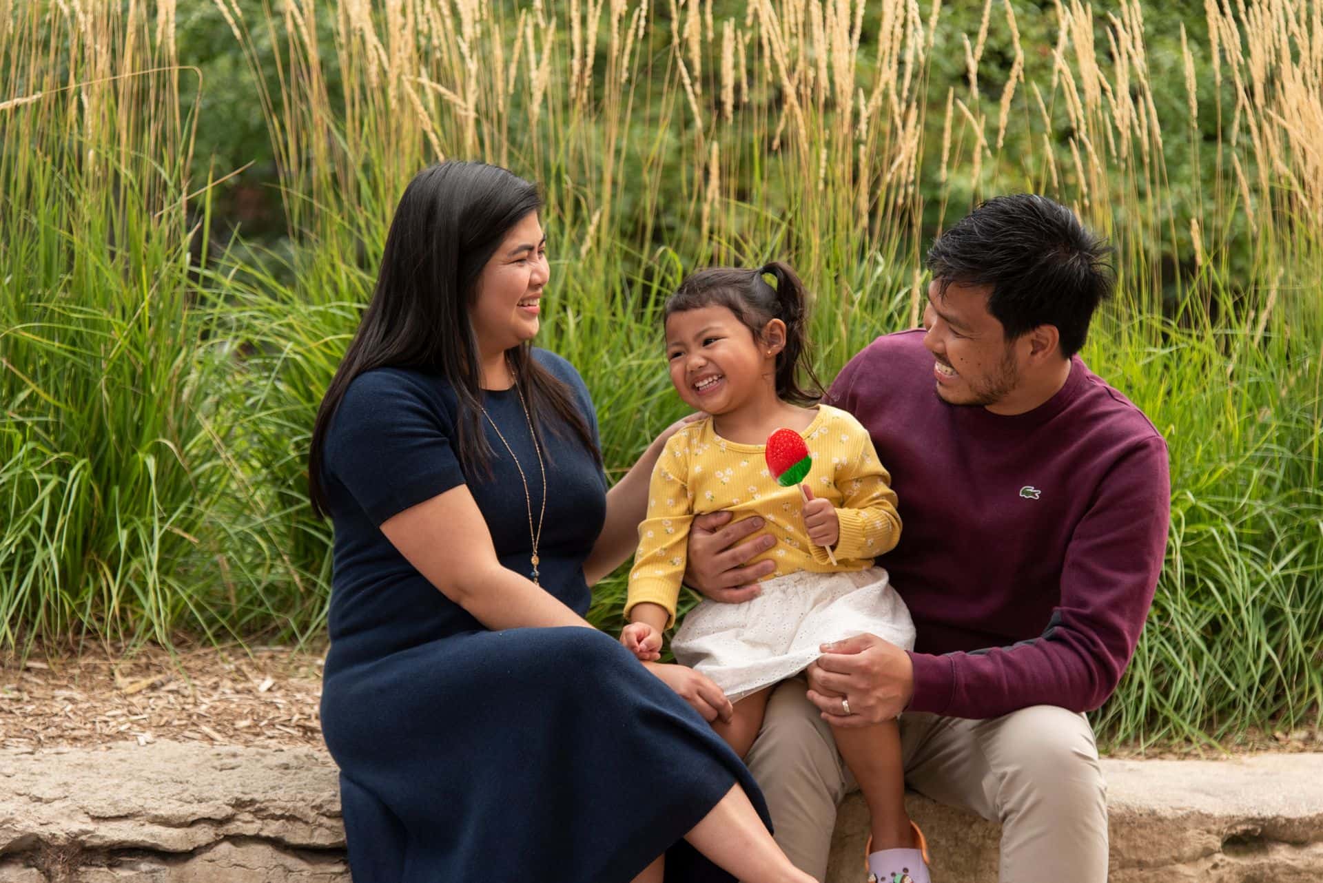 A family of three laughing as they sit in the village. 