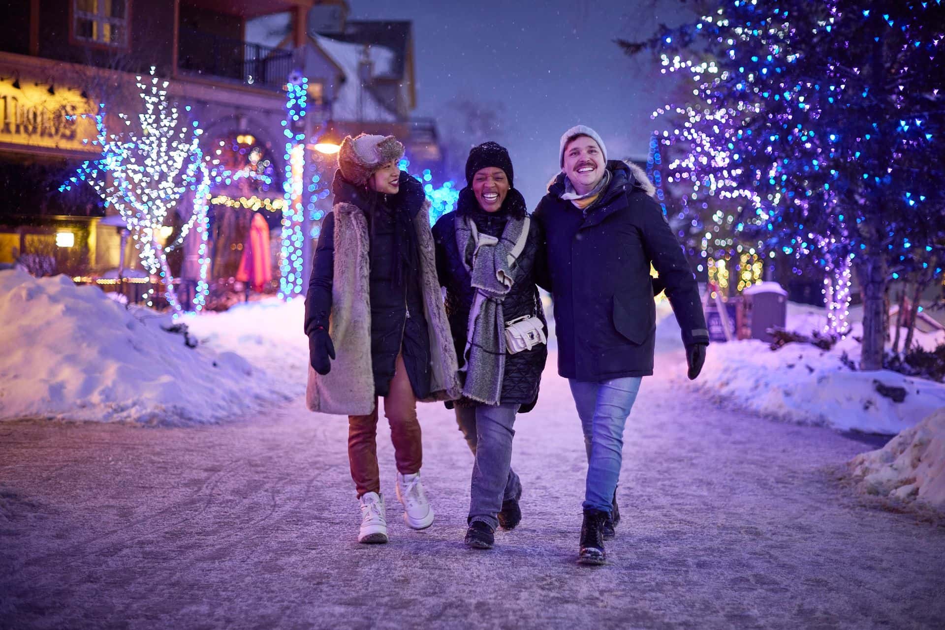 Group of adult friends laughing while strolling through the snow covered streets, taking in the Holiday Magic Light Trail