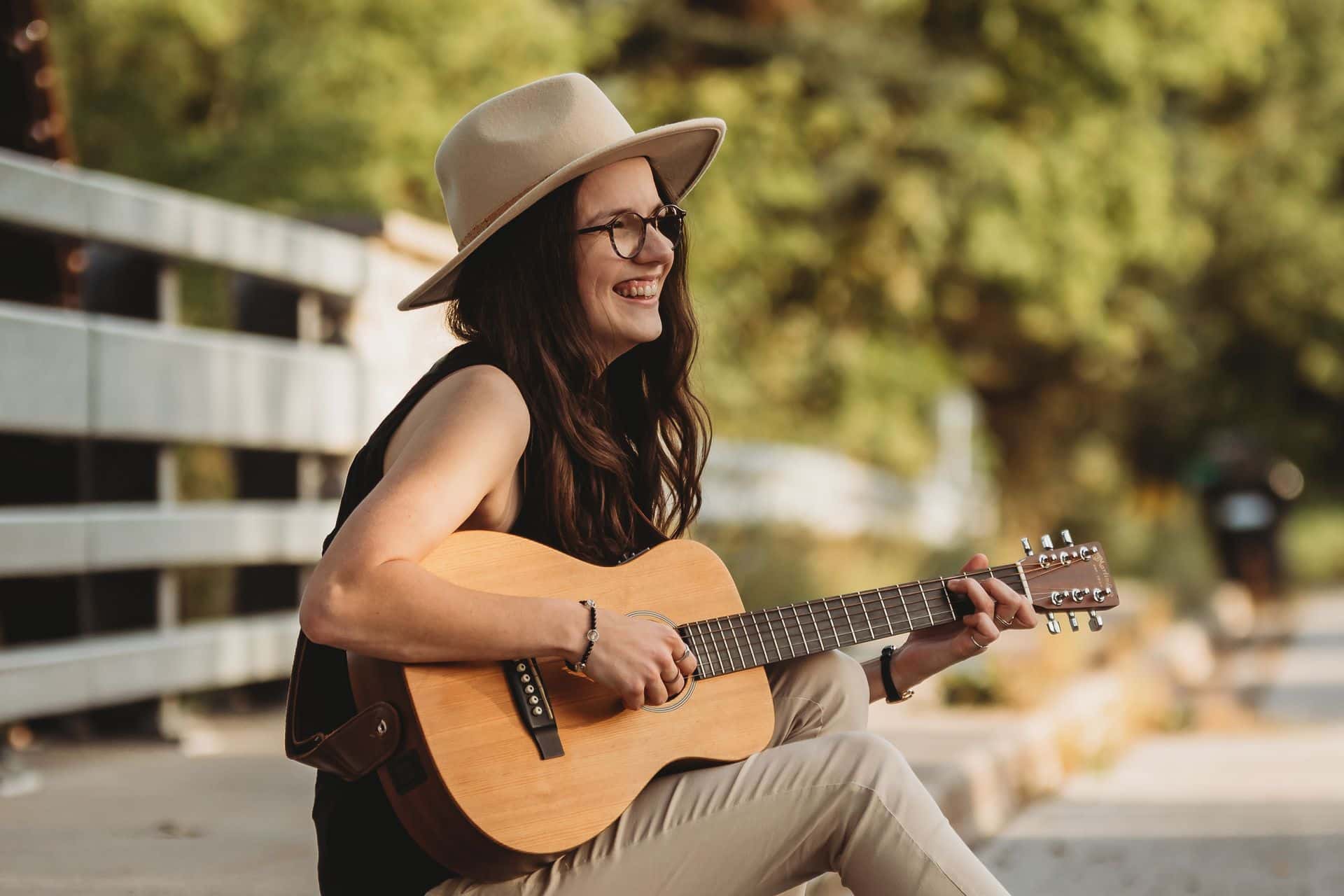 Side profile shot of singer, Jess Bowman, smiling and playing her acoustic guitar