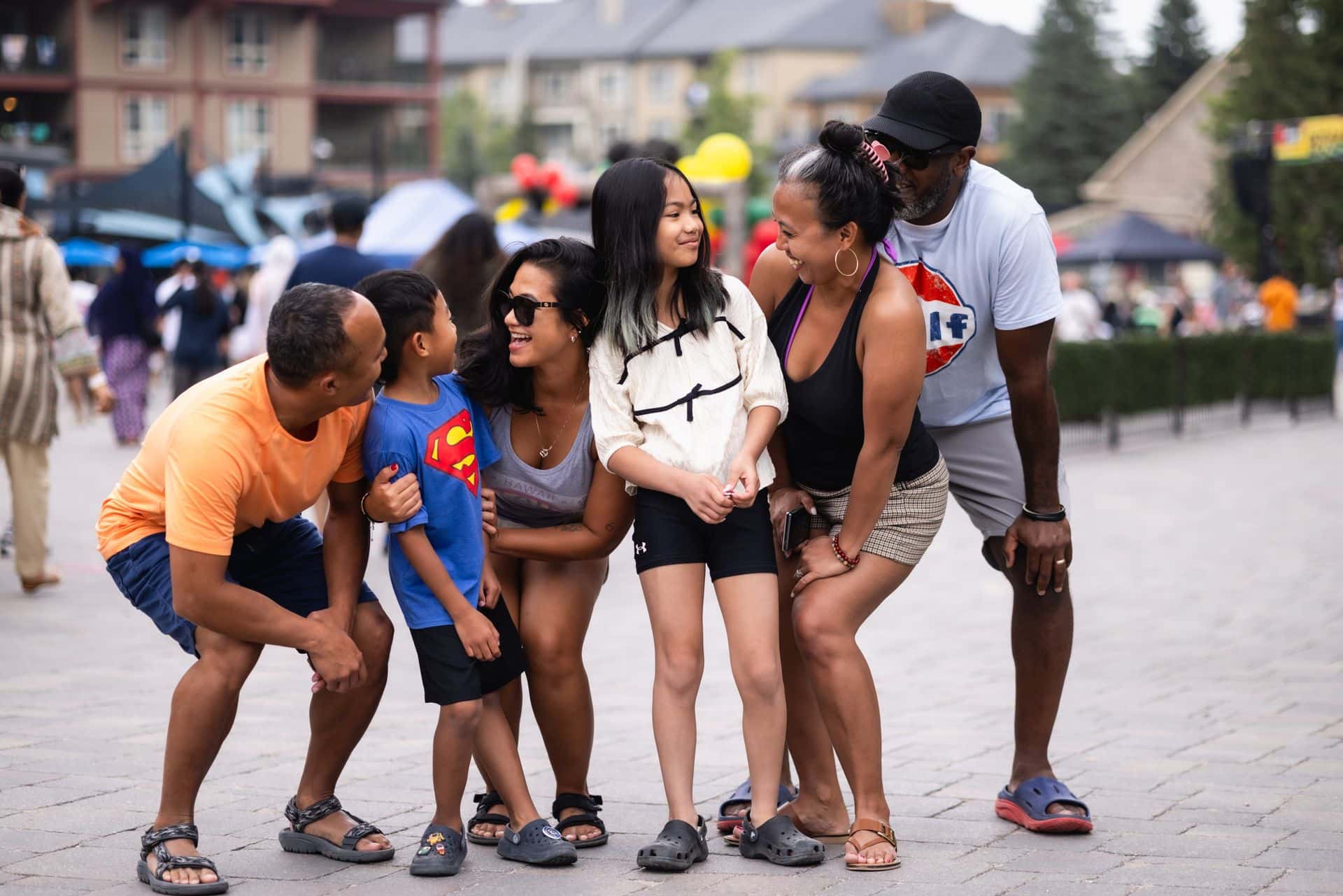 A group of family friends laughing and looking at each other during a summer photoshoot in the Village Events Plaza.