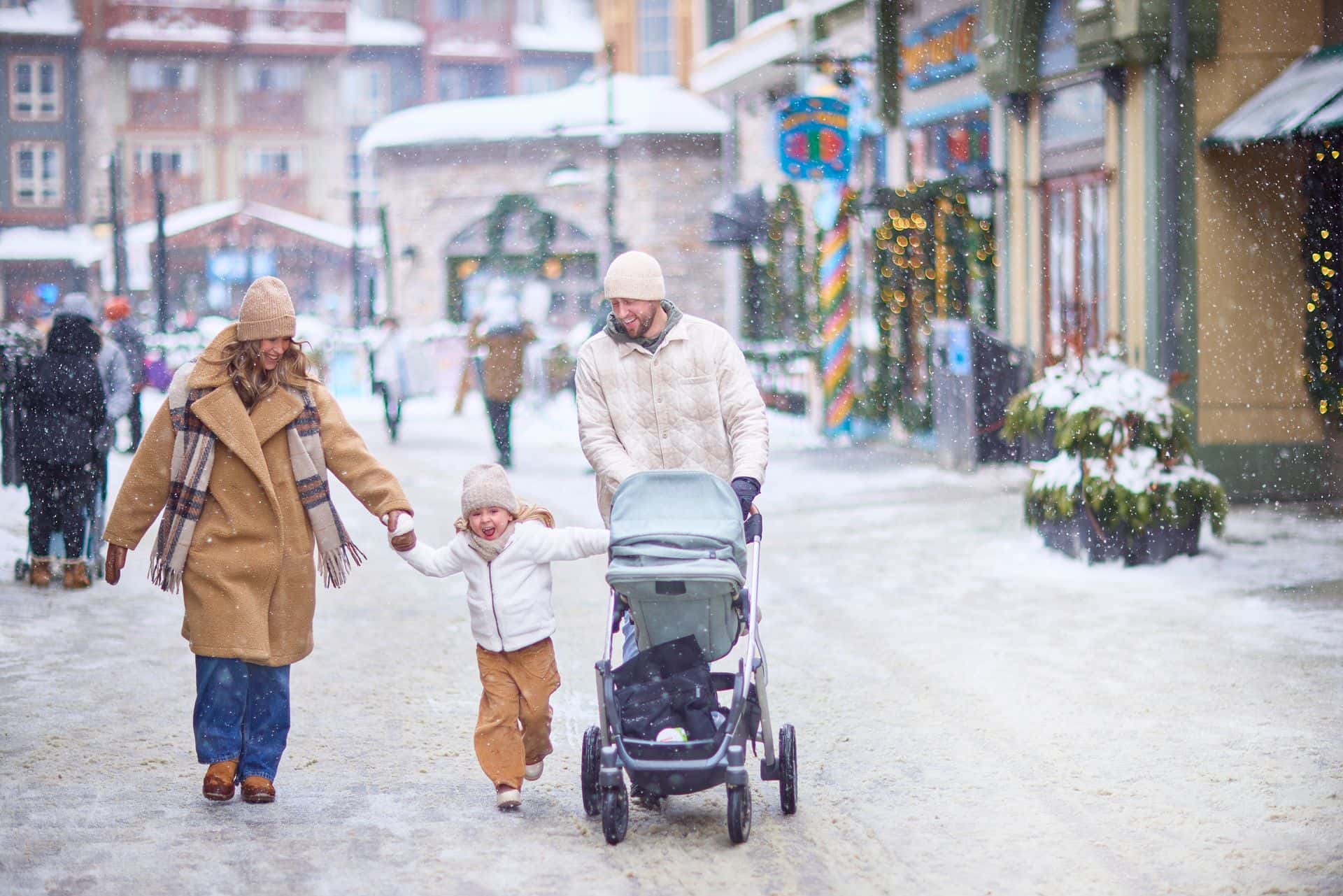 Family of four strolling through the festively lit pedestrian Village, all holding hands while dad pushes the stroller.