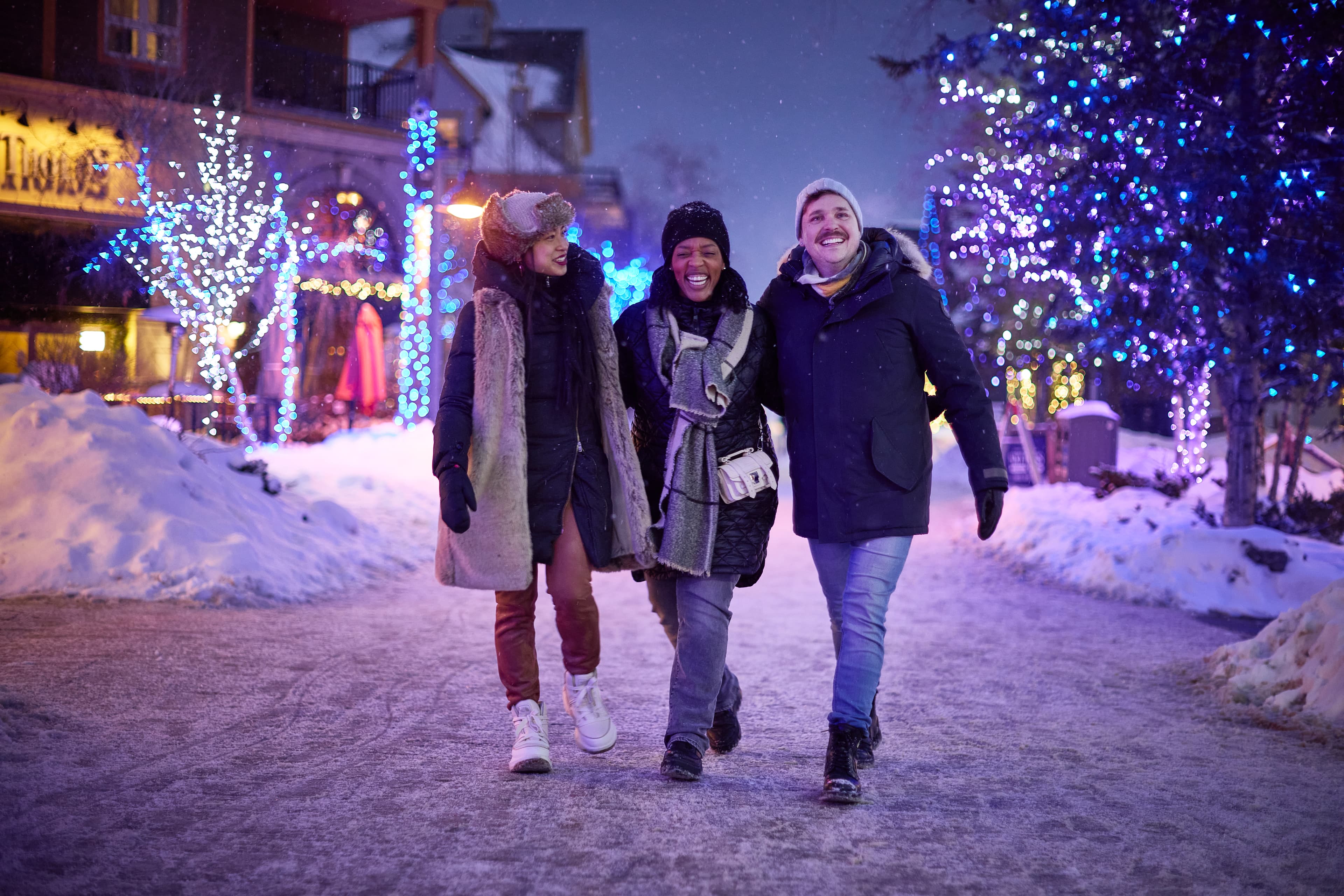 Group of adult friends laughing while strolling through the snow covered streets, taking in the Holiday Magic Light Trail