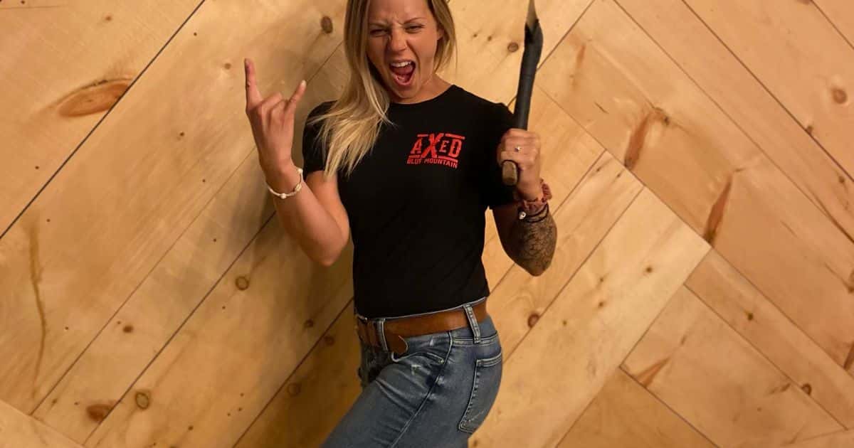 A woman standing with axe in one hand and giving rock n roll horns in the other at Axed at the Bunker
