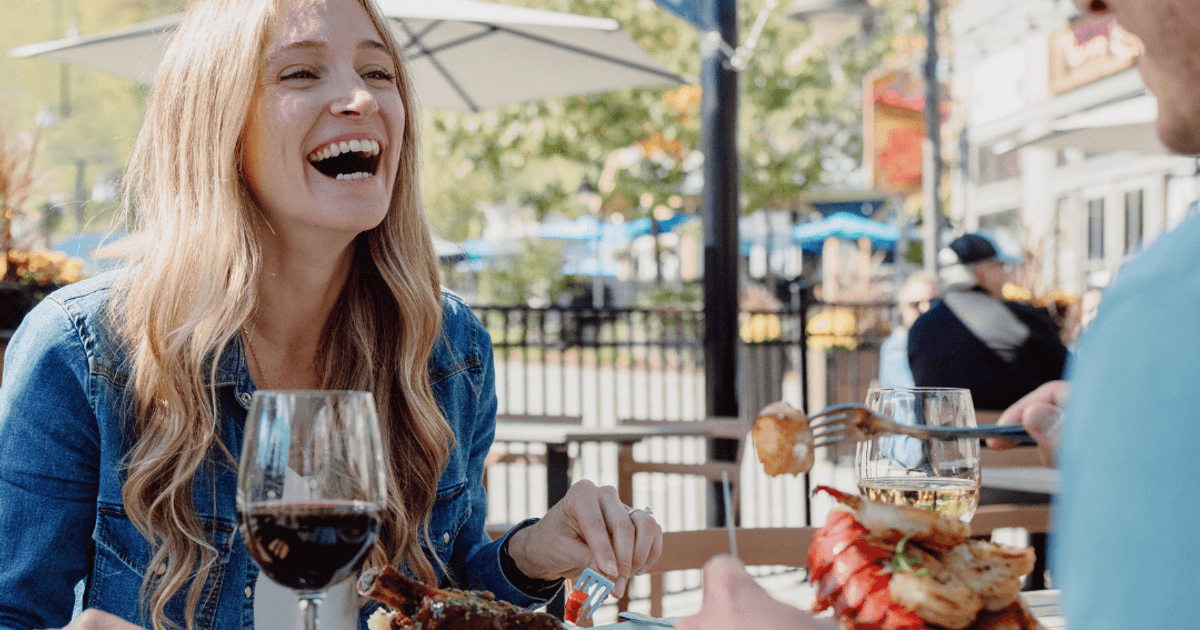 A woman laughing while on a sun soaked patio with their partner, enjoying seafood platters and wine at Copper Blues.