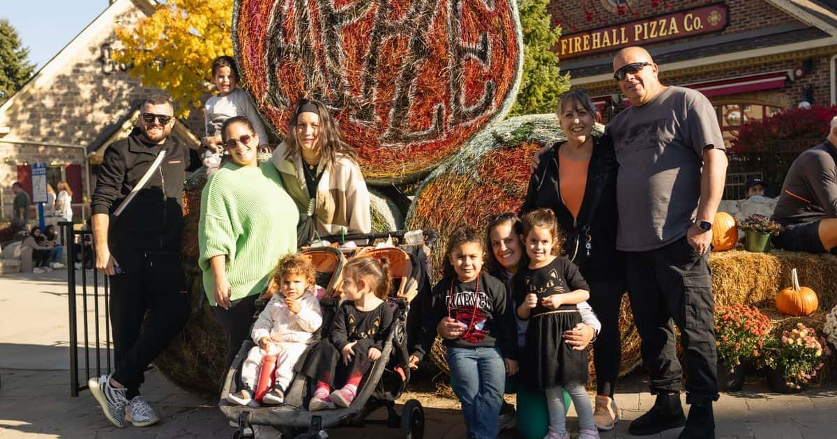 An extended family gathers together for a fall group photo in front of the decorated hay bales for Apple Harvest Festival Weekend in the Village