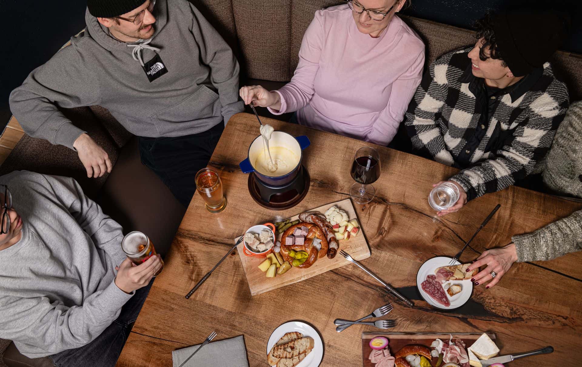 A group of friends gathered in a booth at The Pottery Restaurant with a table full of classic fondue and things to dip in it.