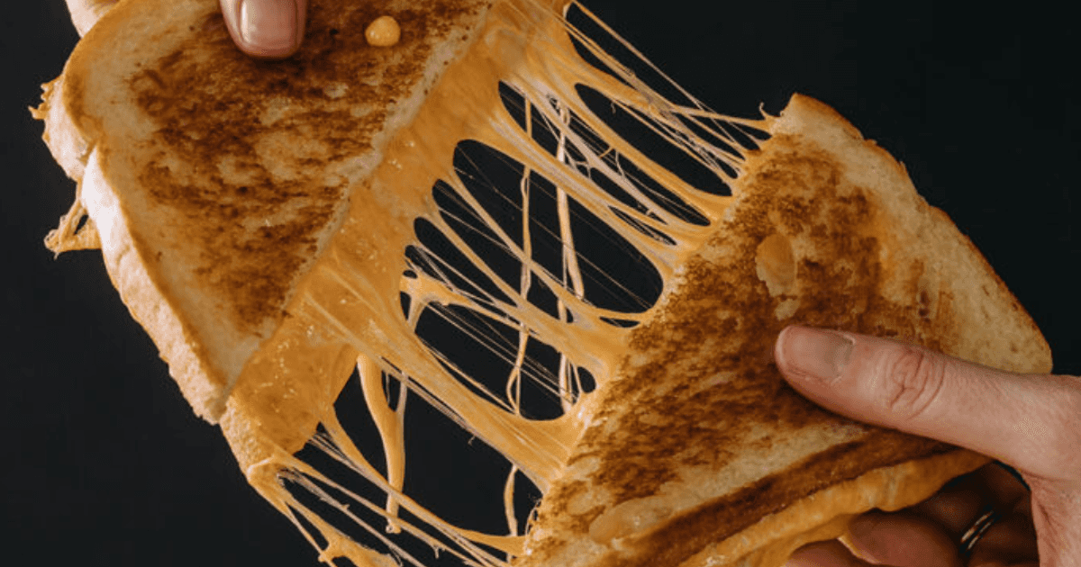 A classic Cheezed sandwich being pulled apart as cheddar and swiss ooze out, giving the ultimate cheese pull.