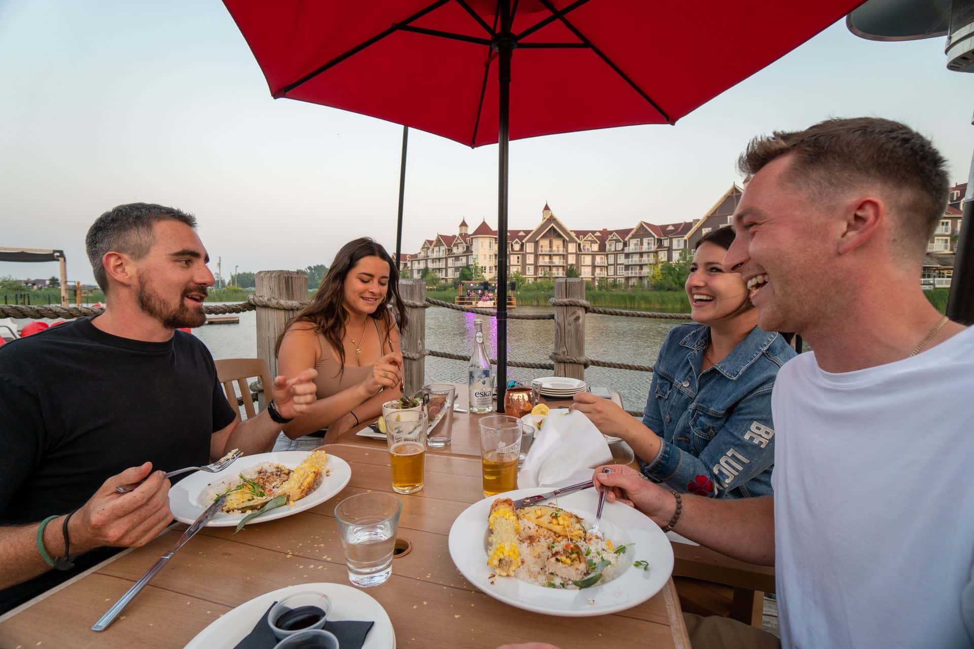 Friends dining on the sun-kissed patio at Kaytoo while enjoying live music on the Floating Stage on a warm summer evening.