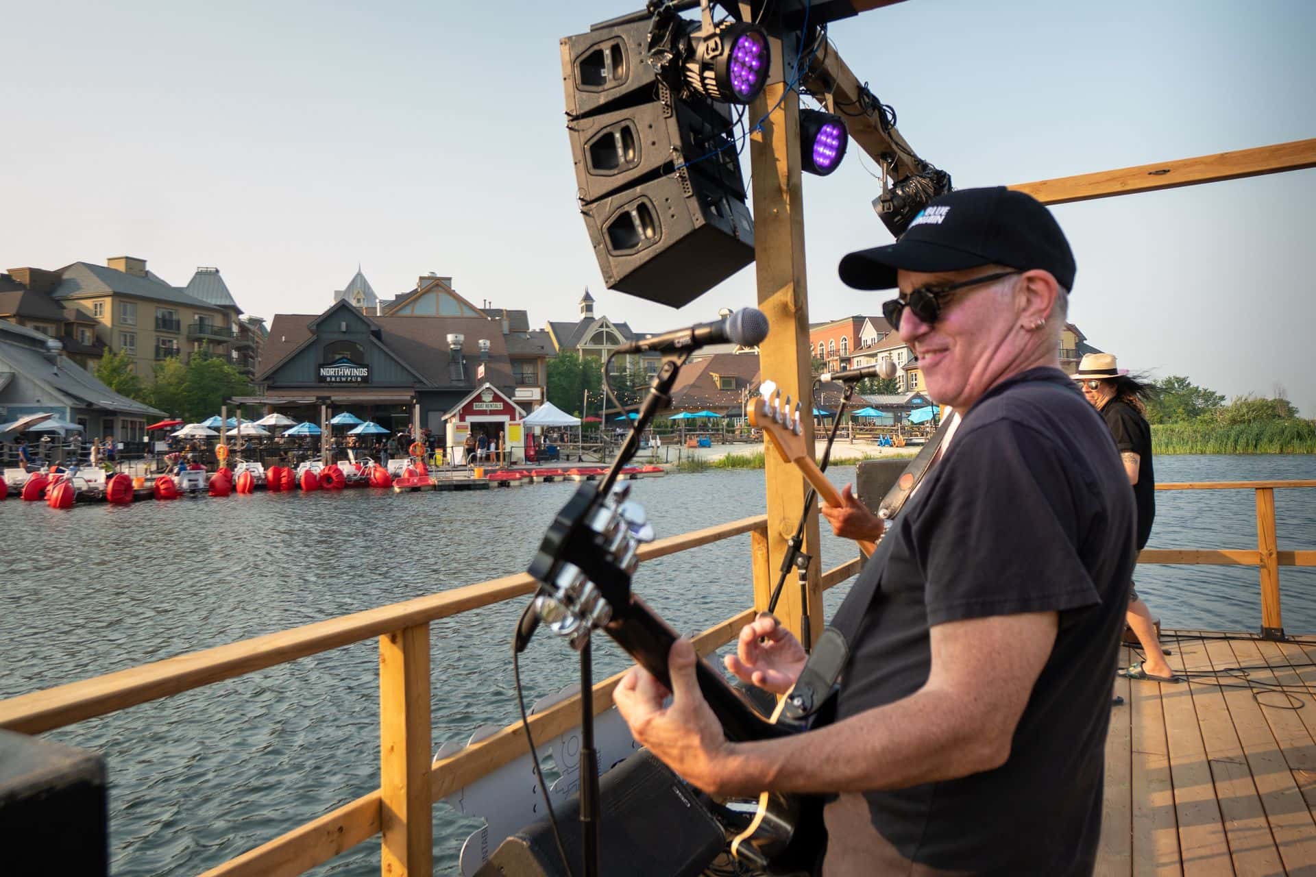 Live band rocking out of the Floating Stage with views of the Village patios on a warm evening at sunset.
