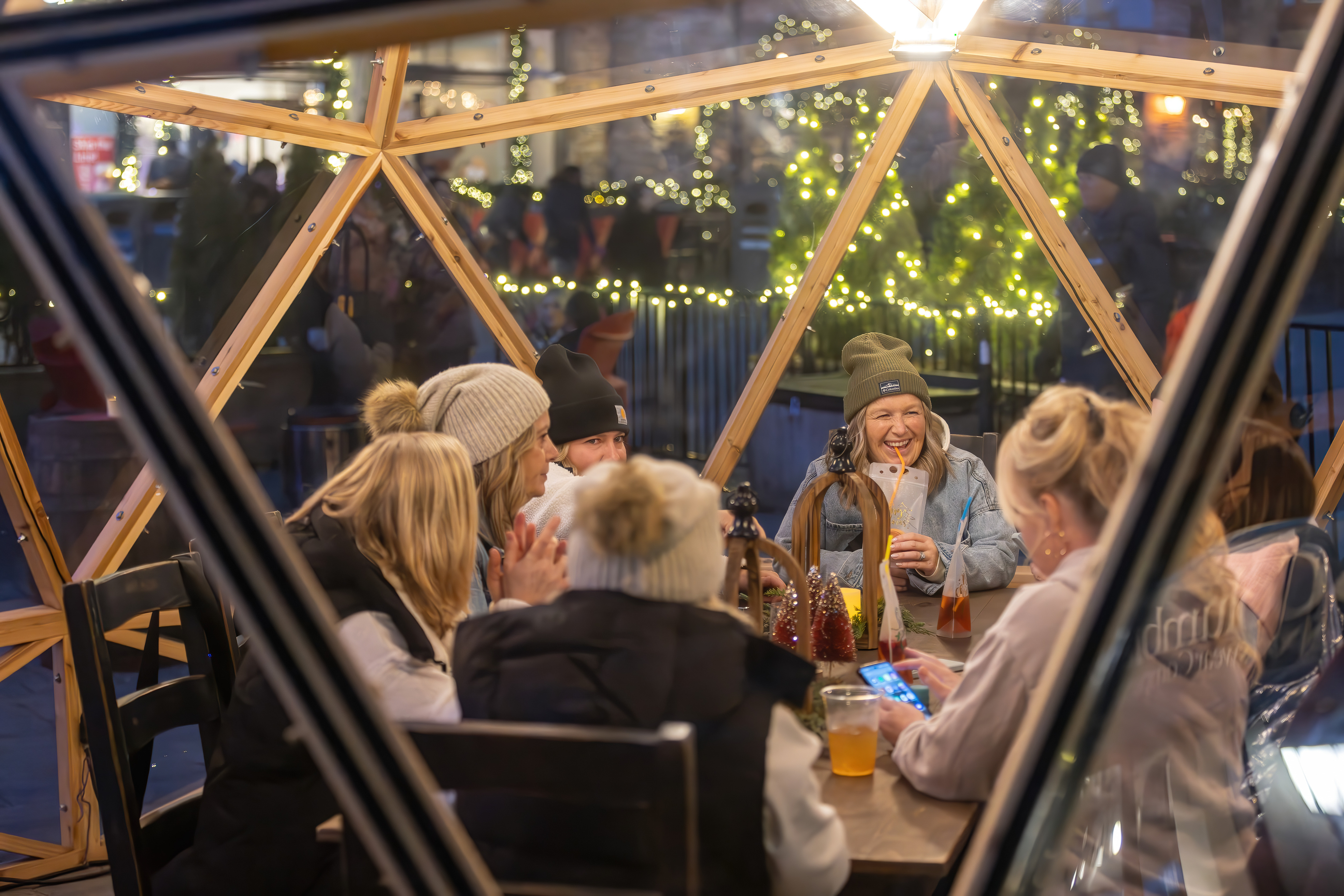 Large friend group laughing and sipping on their festive cocktails together inside a lit Snowdome.