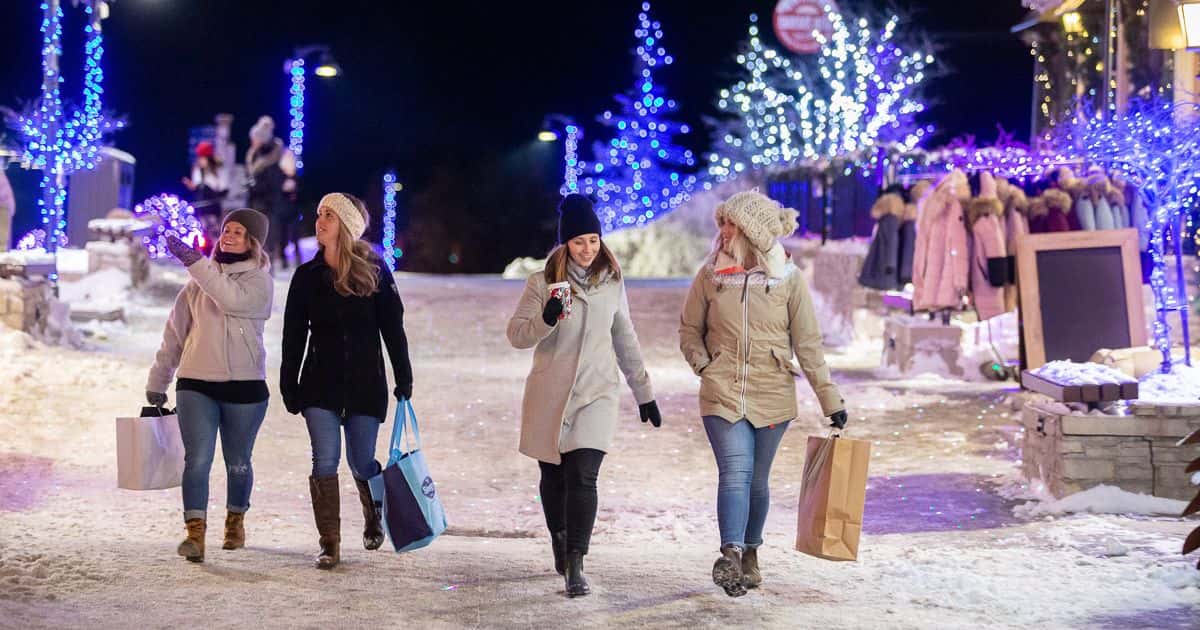 Group of four friends shop the Village as they stroll through the festively lit Holiday Magic Light Trail.