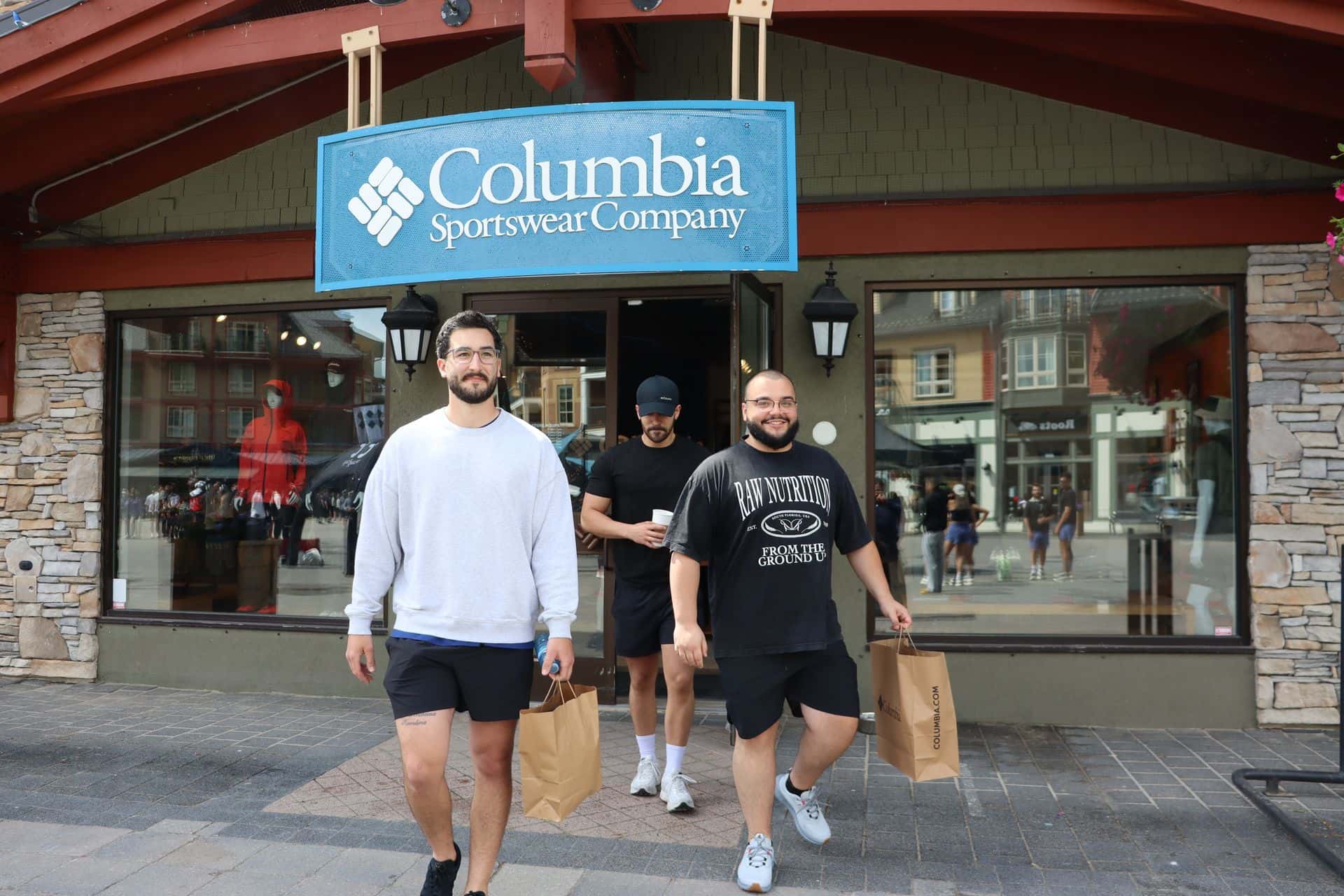 3 guys walking out of the Columbia Sportswear store front carrying shopping bags.