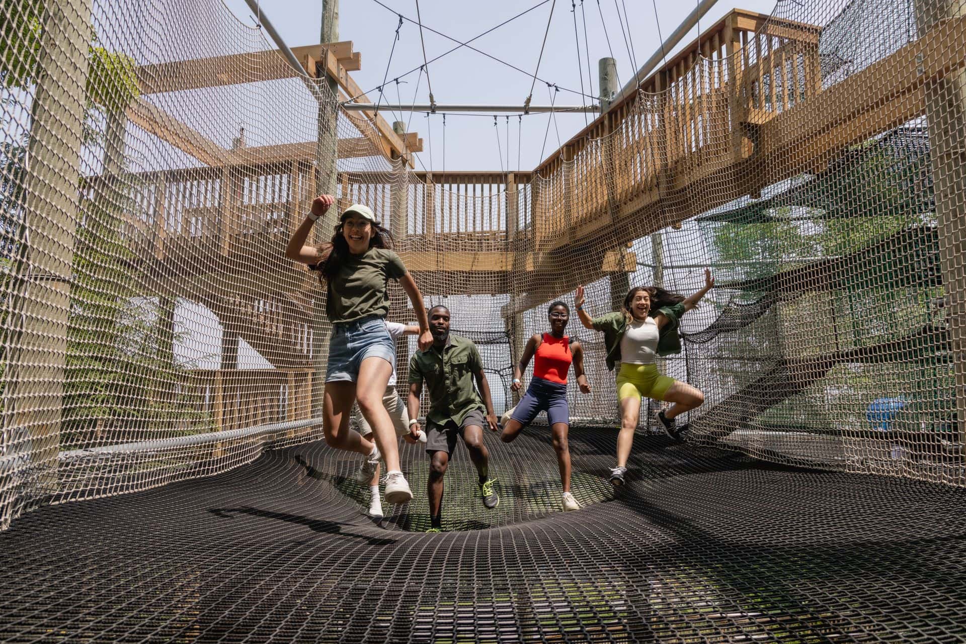 A group of kids jumping through the trampoline floors of the canopy climb adventure in the Blue Mountain Resort Adventure Park.