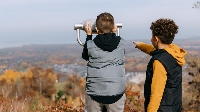 Two young boys take turns looking out the binoculars at the top of the Mountain, gazing out over the amber and auburn leaves on a crisp fall afternoon.