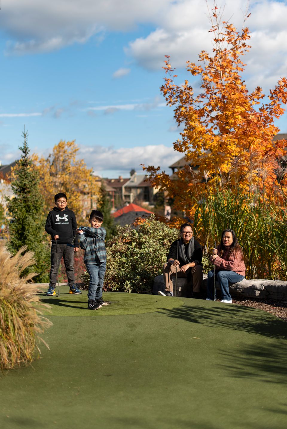 A family of four playing a game of mini putt at the Cascade Putting Course at Blue Mountain on a sunny Fall afternoon, surrounded by the beautiful amber and auburn leaves.