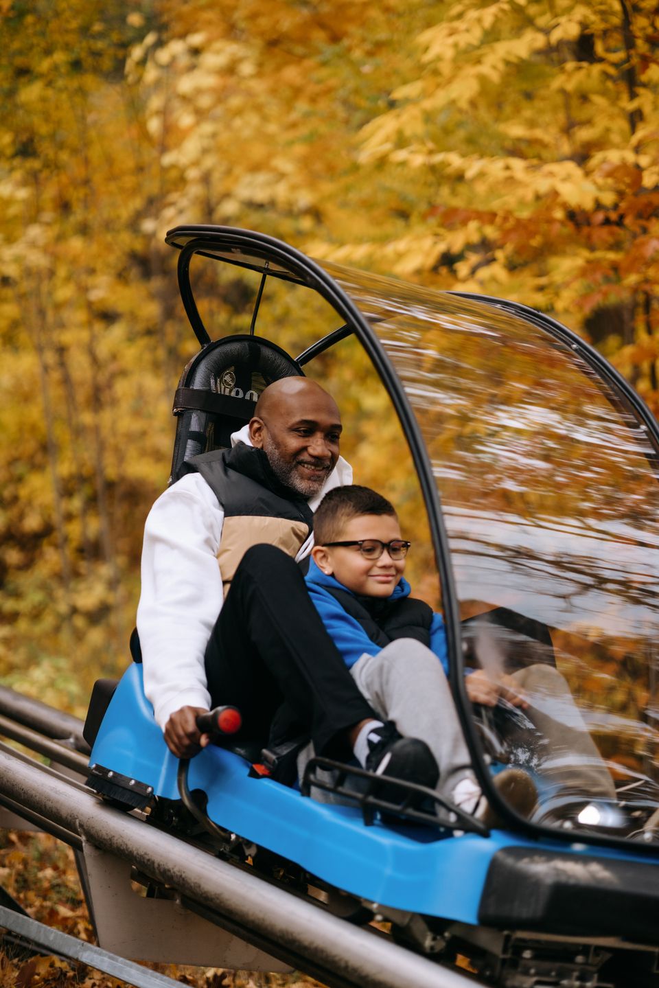 A father and son zoom down the fall leaves on the mountain riding the Ridge Runner Mountain Coaster at Blue Mountain.