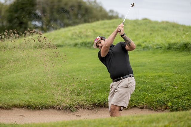 A man shooting his ball out of the sand trap on a summer day at Monterra Golf Course at Blue Mountain Resort.