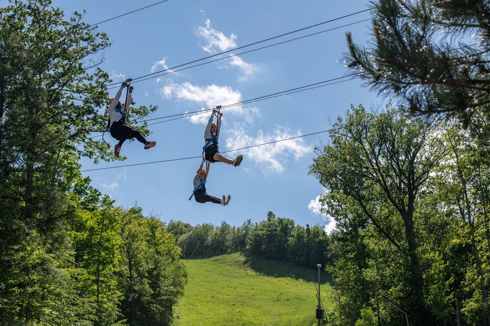 3 adventurers flying through the trees along the Wind Rider Triple Zips ziplining at Blue Mountain Resort.