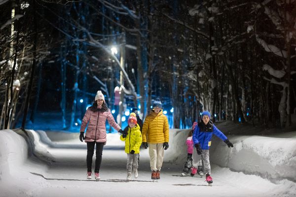 Mom takes her kids skating under the festively lit Woodview Skating Loop at the top of the Mountain on a Winter's night.