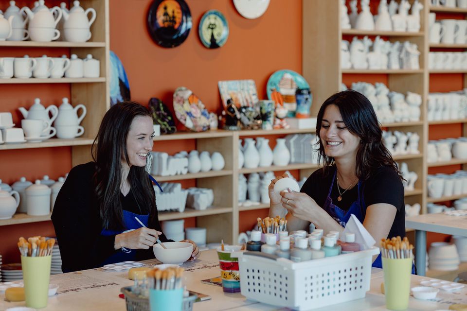 Two girlfriends painting their own pottery inside the cozy Crock-a-Doodle studio in Blue Mountain Village.