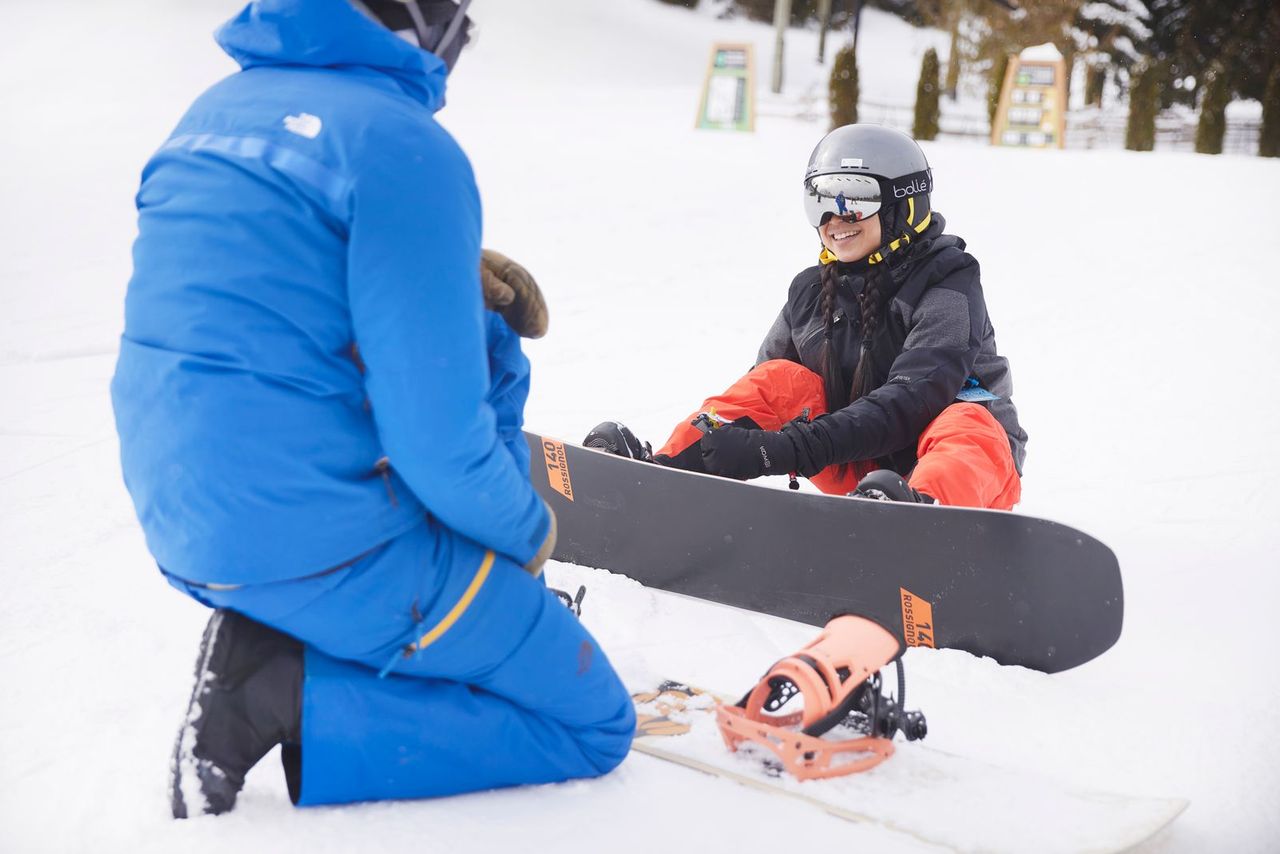 A beginner snowboarder does up her bindings.