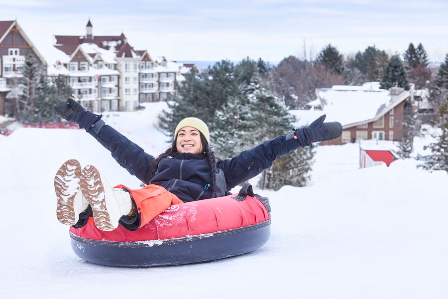 Woman in a snow tube, smiling with hands in the air as she slides down the snow covered slope.