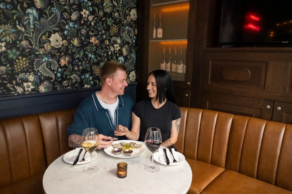 A couple gazing into each other's eyes, enjoying a fine dining experience with oysters and wine at Twist Kitchen & Cocktail in the Village