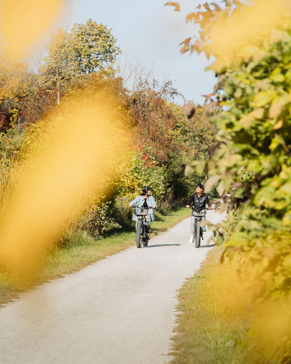 Two women zipping along the Georgian Trails on their e-bikes during a sunny Fall afternoon in The Blue Mountains.