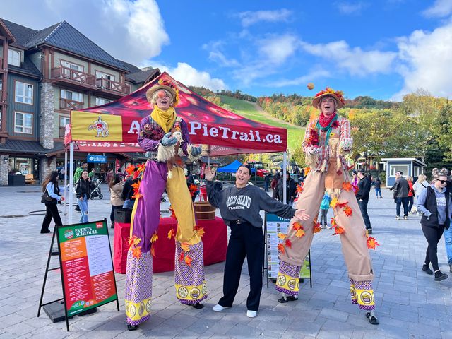 Two scarecrows on stilts pose at the Apple Pie Trail tent on a sunny Fall afternoon in the plaza for Apple Harvest Festival Weekend
