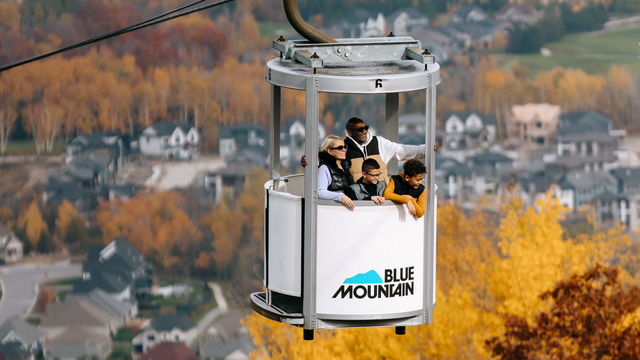 A family of four ascends up Blue Mountain Resort on the Open-Air Gondola, taking in the stunning views of the fall foliage and forests below. 