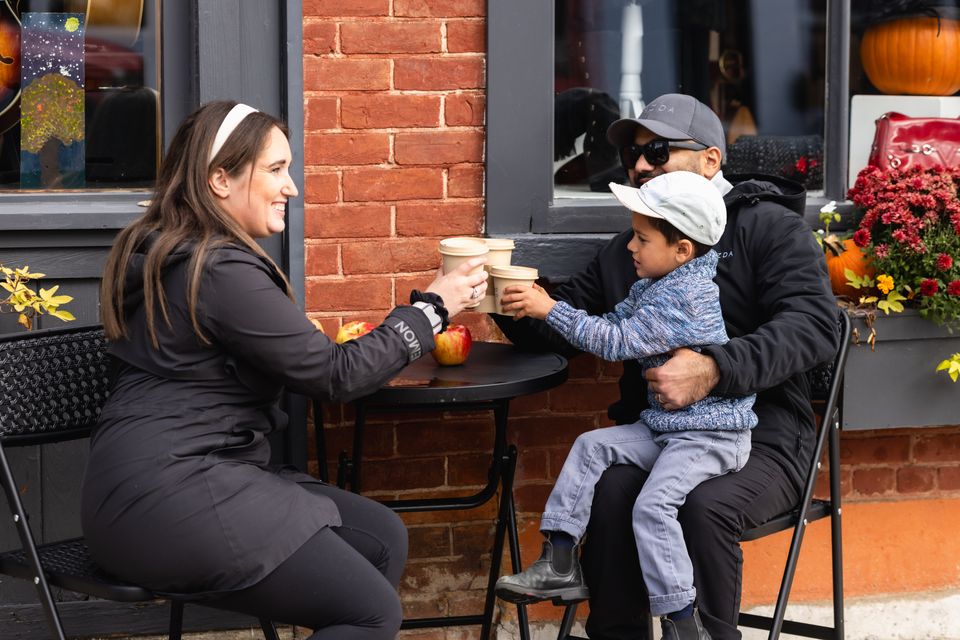 A mom and dad clink together hot drinks with their young son on a Fall family outing in Clarksburg, part of the Apple Pie Trail.