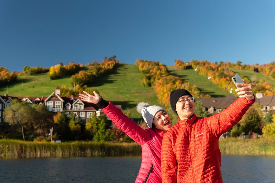 A couple taking a selfie near the mill pond, with the fall foliage cascading across the mountain behind them.